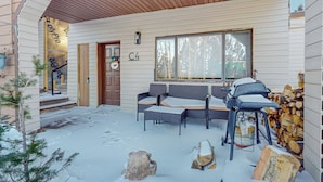A covered outdoor seating area with a sofa and chairs, a grill, and a stack of firewood. - Cozy ski in ski out studio in Angel Fire!  (Angel Fire)