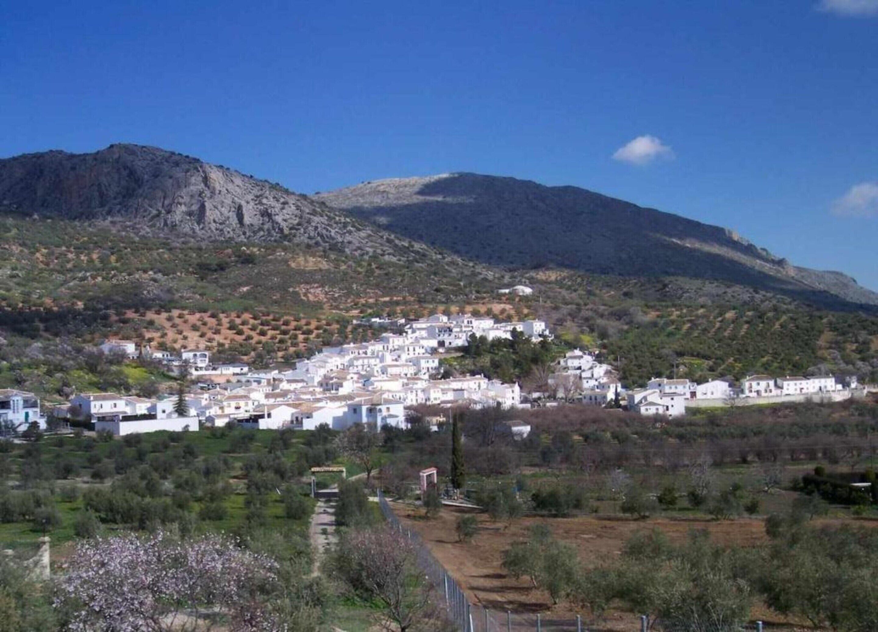A hillside village with white buildings, a clear sky, and a mountain in the background.