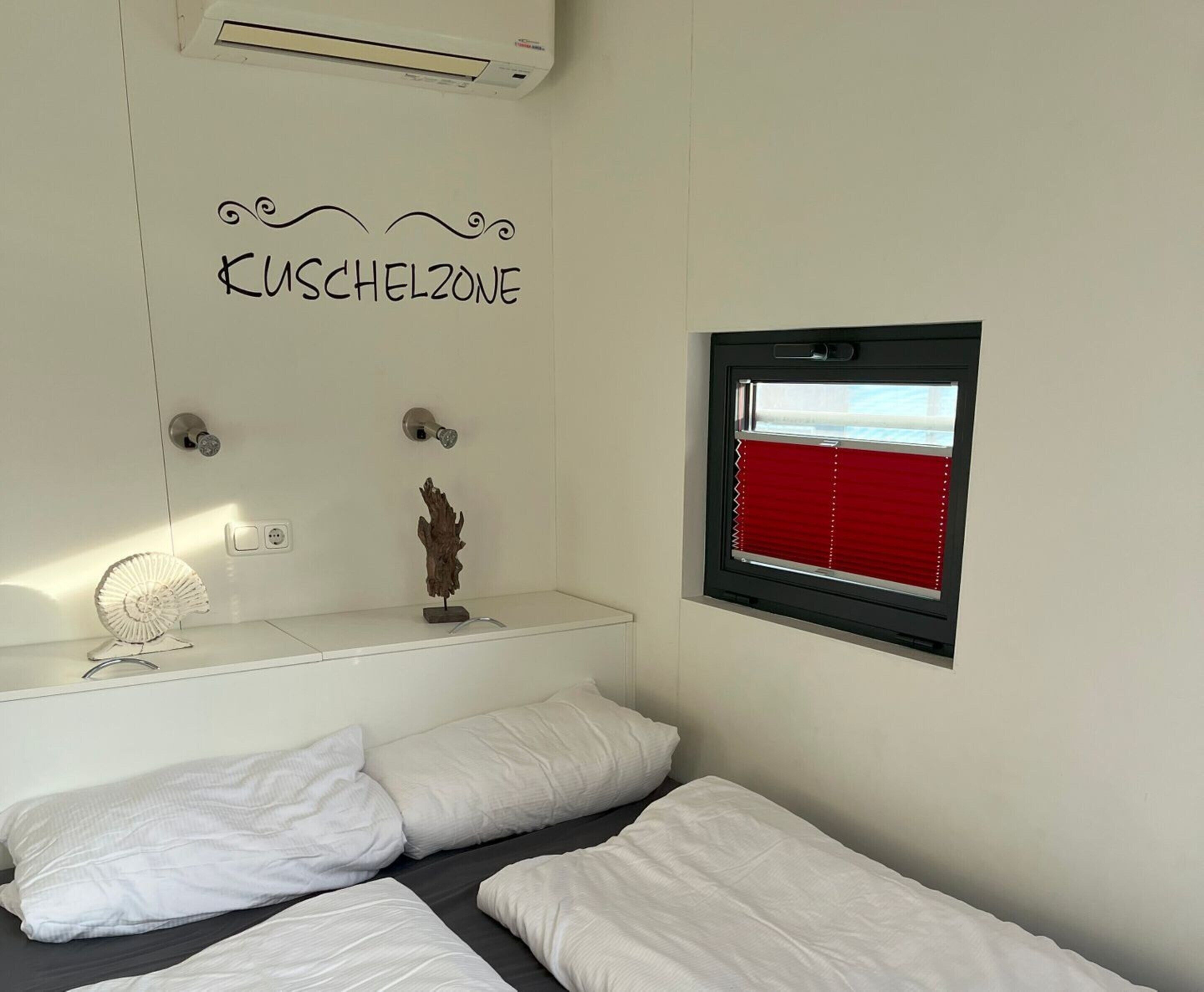 A bedroom with a bed, a window with red blinds, a wall-mounted air conditioner, and a decorative piece above the bed.