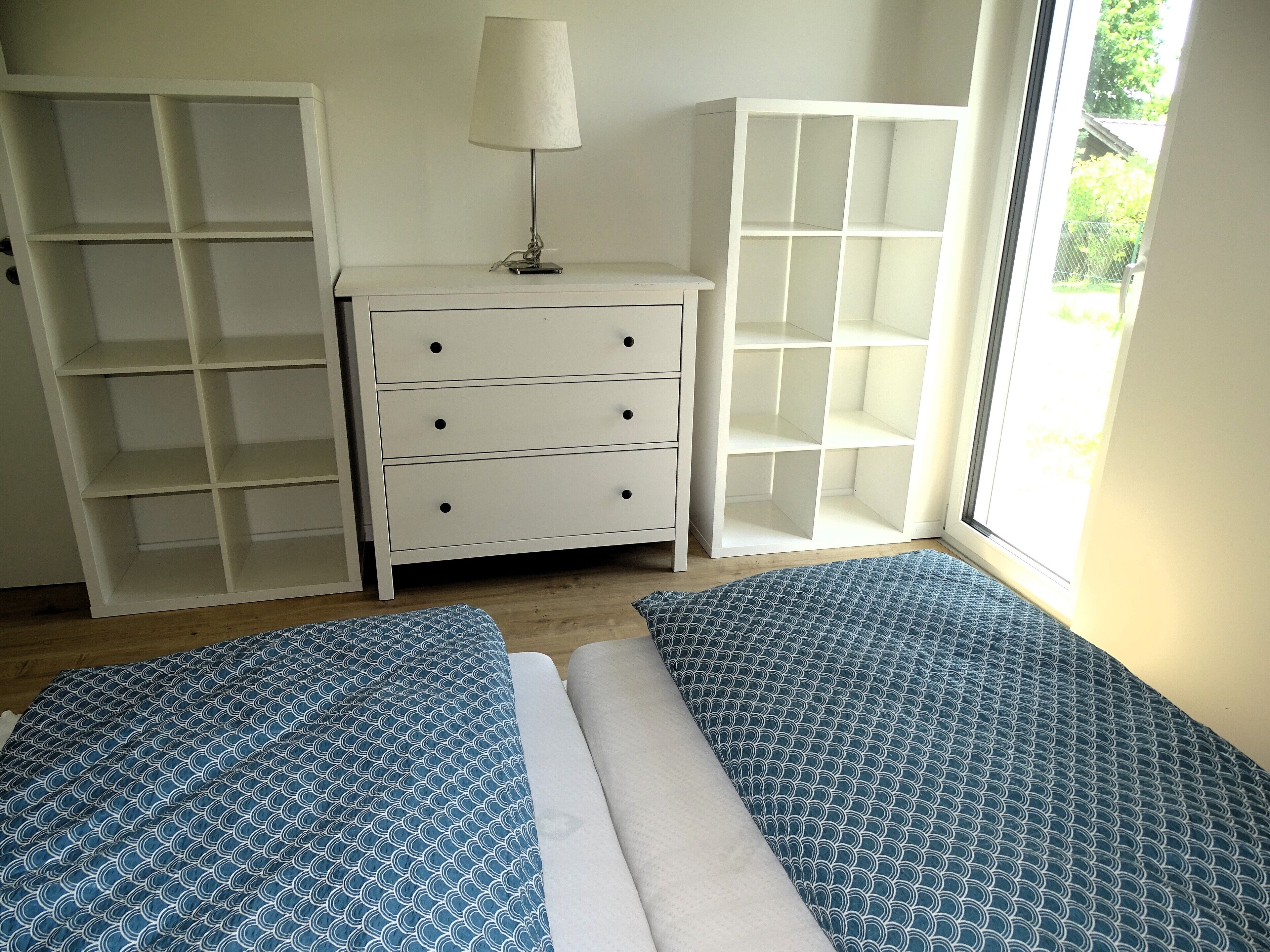 Une chambre avec deux lits, une commode et deux étagères ouvertes.