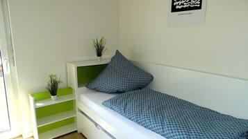 A neatly arranged bedroom with a bed, a bedside table with a plant, and a green storage unit.