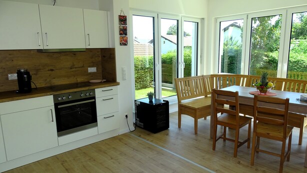 A modern kitchen with white cabinets, a wooden countertop, and a dining area with wooden chairs and a table. - Sunny apartment with large garden in a local recreation area  (Postmünster)
