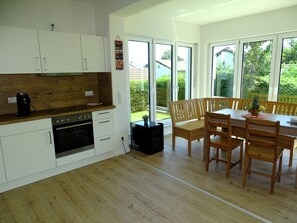 A modern kitchen with white cabinets, a wooden countertop, and a dining area with wooden chairs and a table. - Sunny apartment with large garden in a local recreation area  (Postmünster)