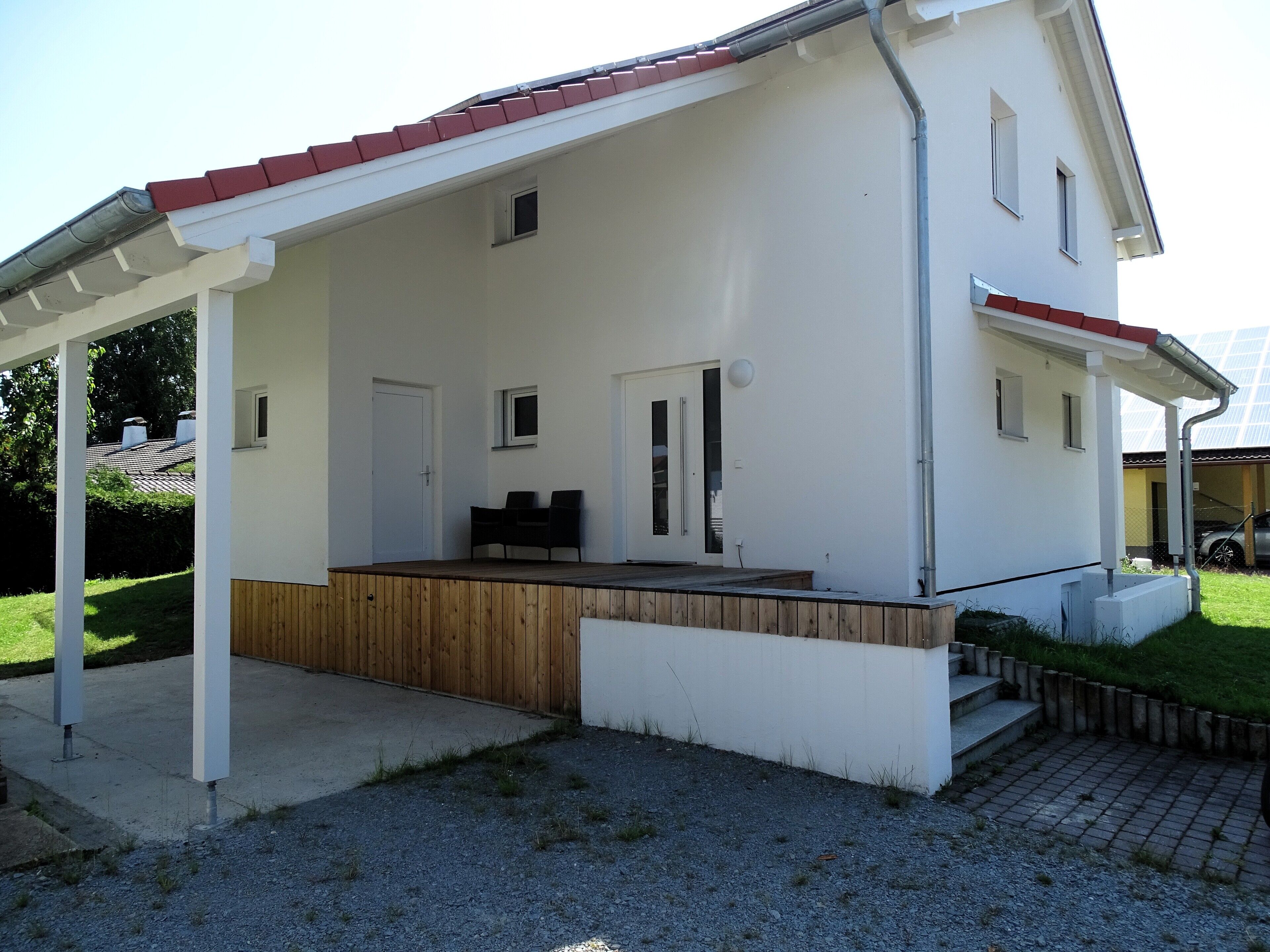A modern house with a covered porch, a wooden deck, and a small garden area.