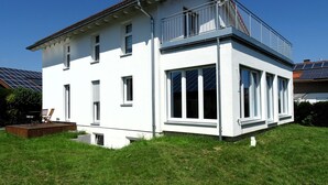 A two-story white house with a balcony, large windows, and solar panels on the roof. - Sunny apartment with large garden in a local recreation area  (Postmünster)