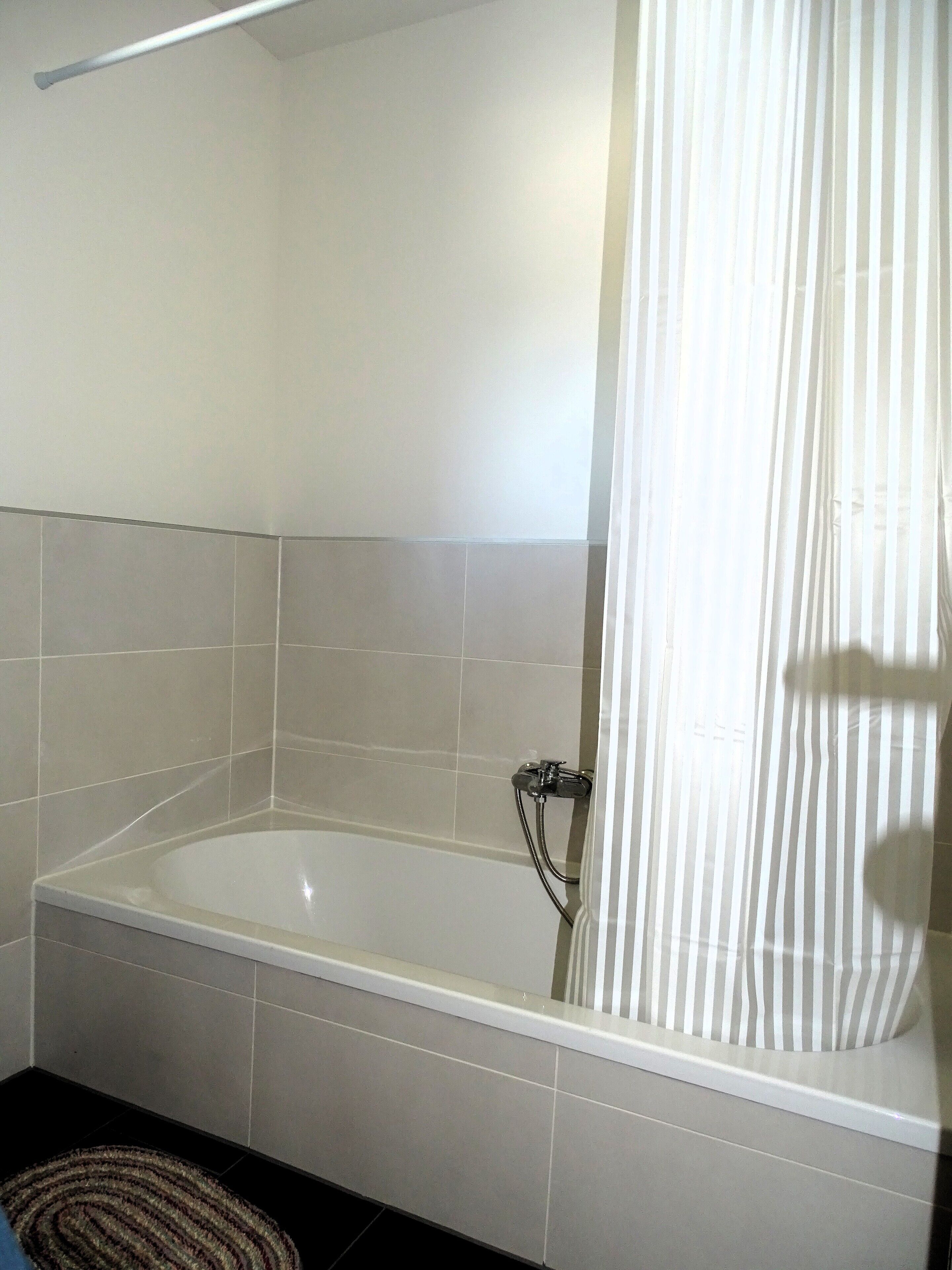 A bathroom with a white bathtub, tiled walls, and a shower curtain.