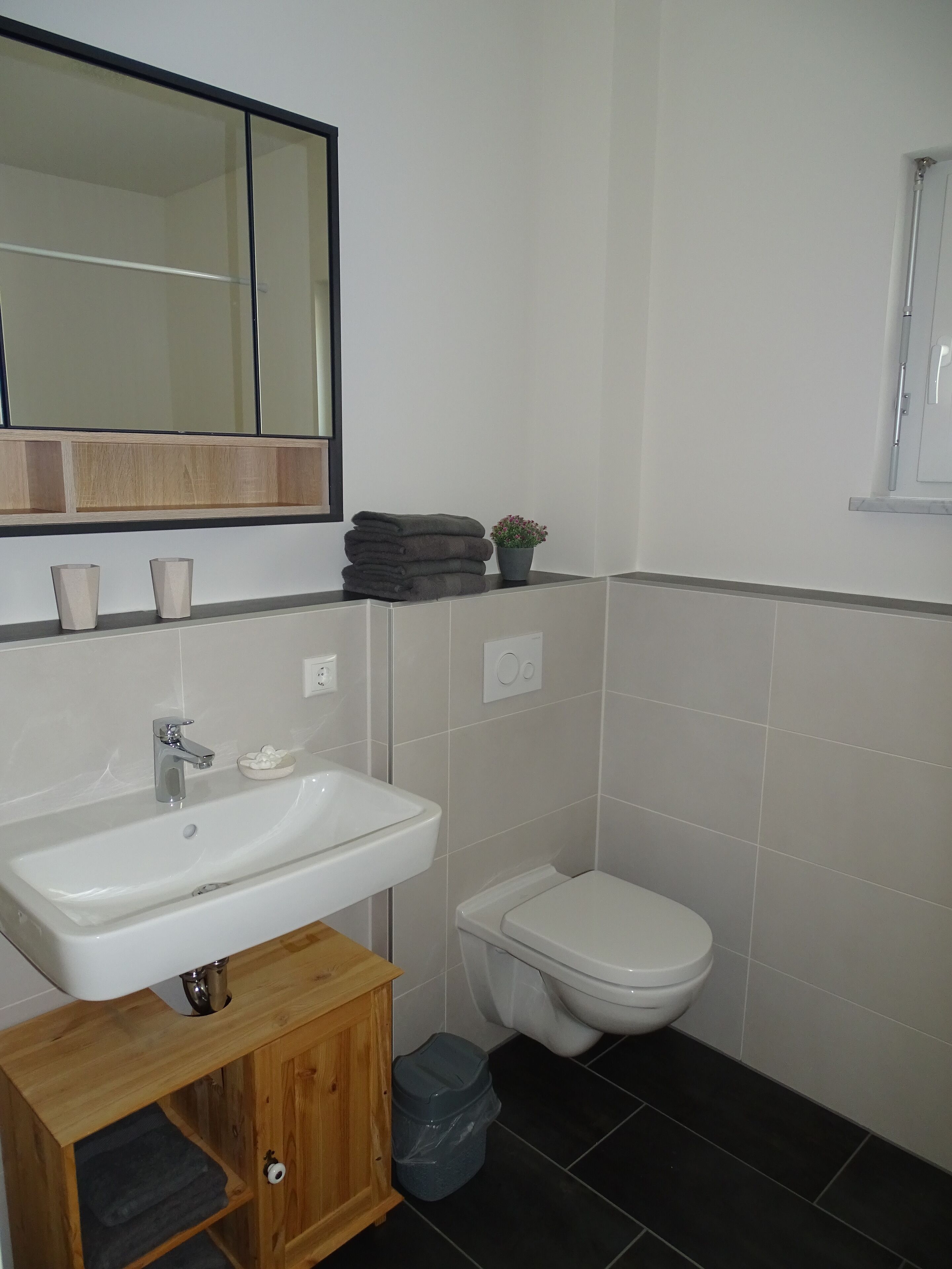 Une salle de bain avec un lavabo blanc, un miroir, des toilettes et une petite poubelle.