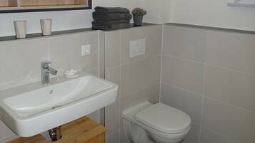 Une salle de bain avec un lavabo blanc, un miroir, des toilettes et une petite poubelle.