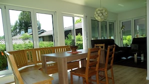 A dining area with a wooden table and chairs, large windows, and a view of greenery outside. - Sunny apartment with large garden in a local recreation area  (Postmünster)