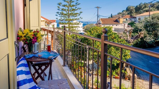 A balcony with a striped sofa, a small table, and a vase of flowers.
