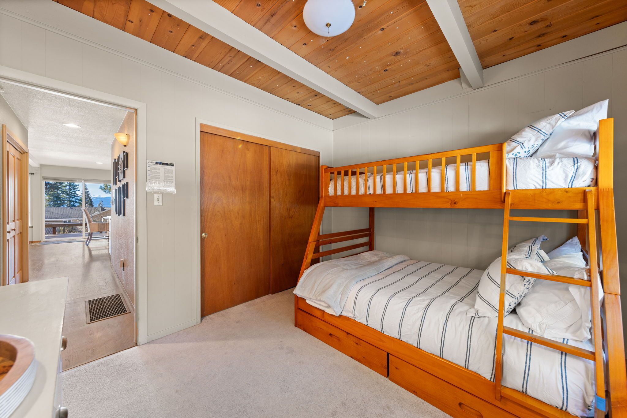 A bunk bed with a wooden frame and white bedding, a wooden door, and a view of a balcony with a railing.