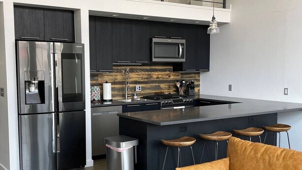 A modern kitchen with a stainless steel refrigerator, microwave, and gas stove. There is a small island with bar stools and a trash can. - Stay at the historic Opera House in downtown Salida! (Salida)