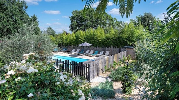 Un jardin à l’arrière de la maison, avec une piscine, entouré d’une clôture en bois et d’une végétation luxuriante.