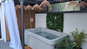 Un espace de détente avec un bain à remous en pierre, un mur en bambou et un rideau blanc.