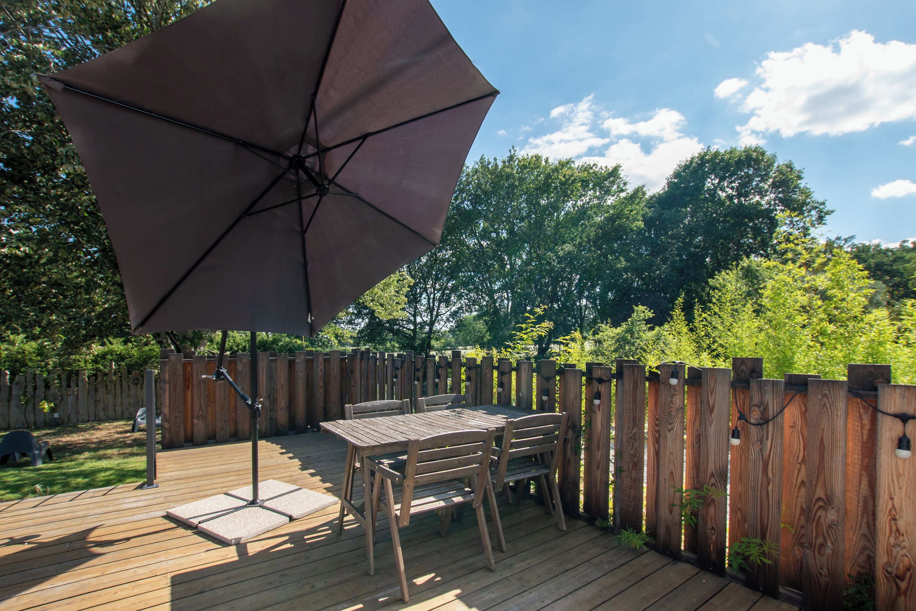 A wooden deck with a table and chairs, a large umbrella, and a wooden fence.