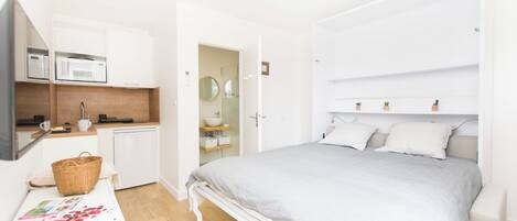 Un dormitorio con una cama, una mesita de noche, un microondas, un lavamanos y una puerta que da a un baño.