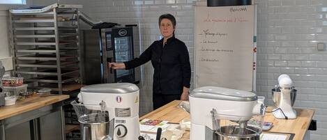Una cocina con electrodomésticos de acero inoxidable, una pizarra con elementos de menú, y una persona de pie junto al mostrador.