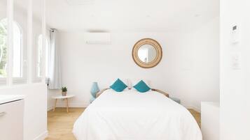 A bedroom with a bed, a round mirror, a small table with a plant, and a window with curtains.