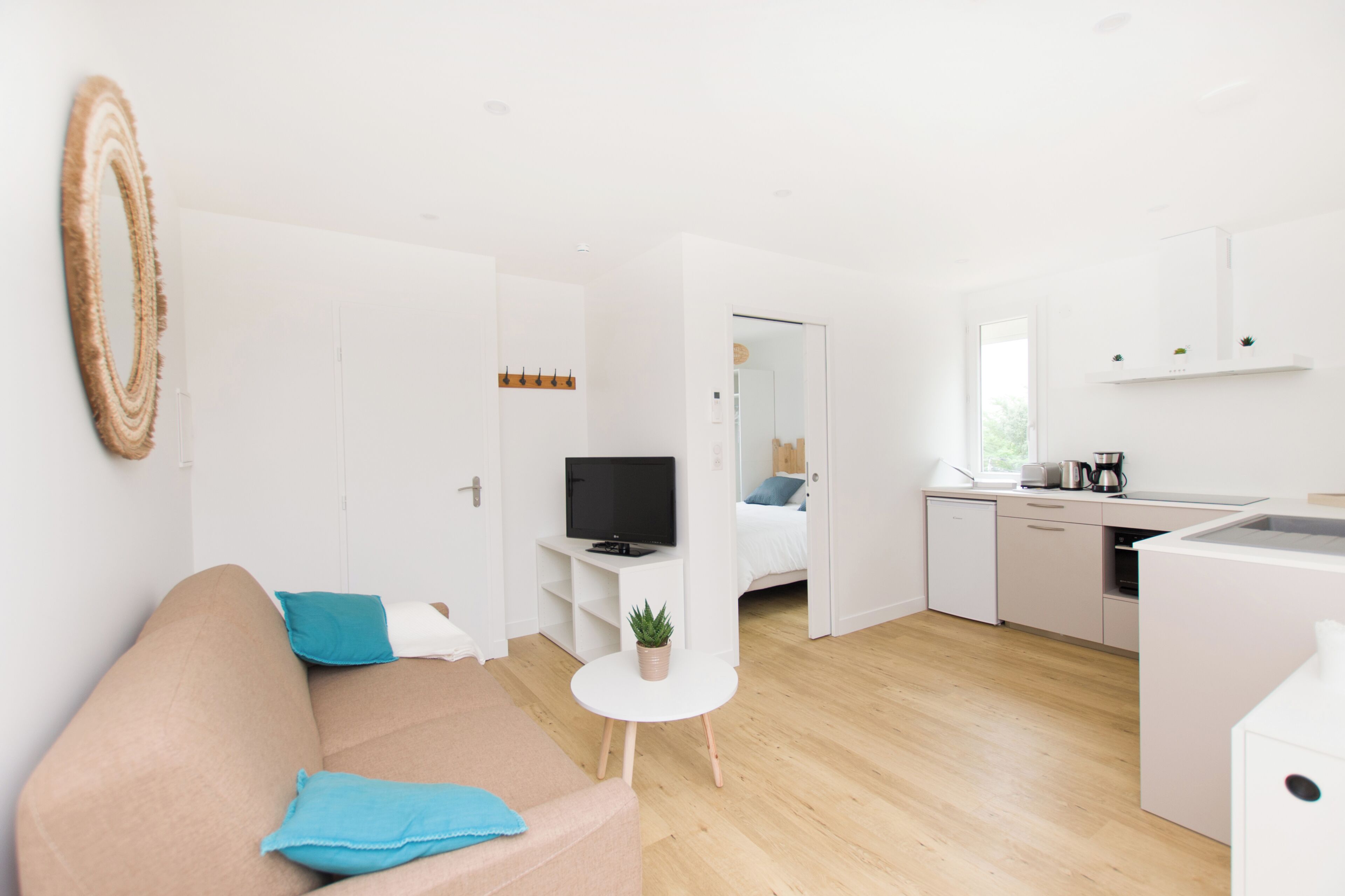 A modern, open-plan living space with a sofa, a small table, a TV, a kitchen area, and a bathroom visible through an open door.