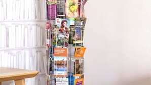 A vertical display of brochures and pamphlets against a white wall, with a wooden table and a grey couch in the foreground. - Maison deco années 70 / 5 p. garden south Tours (Joué-lès-Tours)