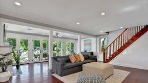 Un salón amplio con un sofá gris, un reposapiés color beige y una escalera que sube al piso superior.