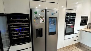A modern kitchen with stainless steel appliances, a built-in wine cooler, and a digital clock on the refrigerator.