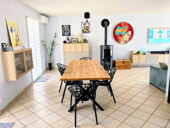 A modern living room with a wooden dining table, black chairs, a TV, and a fireplace.