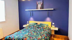 Een slaapkamer met een bed, nachtkastje, wandplank en een plafondlamp.