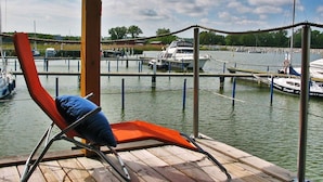 A wooden deck with a lounge chair and a view of a marina with boats. - Hausboot in Barth am Barther Bodden (Barth)