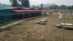 A covered outdoor seating area with tables and benches, surrounded by a fence and greenery. - RASS Resort (Karjat)