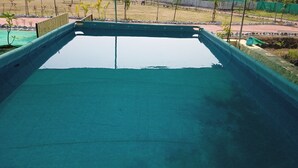 A rectangular swimming pool with a green border and a flat surface. - RASS Resort (Karjat)
