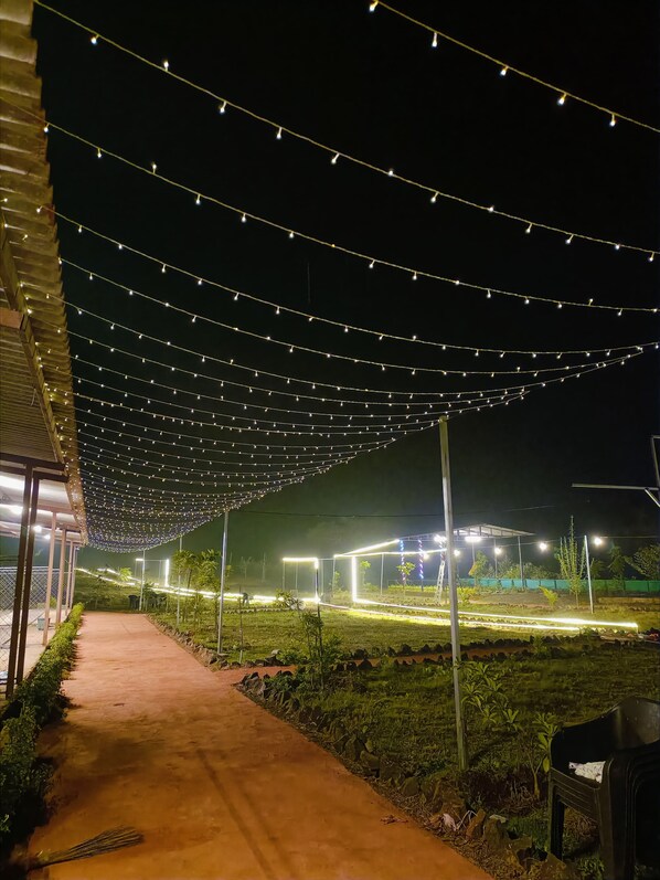 A pathway lined with string lights and a covered area with a view of a landscaped garden. - RASS Resort (Karjat)