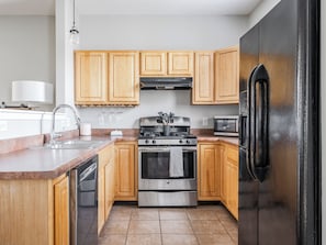 A kitchen with wooden cabinets, stainless steel appliances, a sink, and a refrigerator. - Cozy Downtown Escape (Indianapolis)