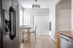 A kitchen with a refrigerator, a dining table with chairs, and white double doors. - Cozy Downtown Escape (Indianapolis)