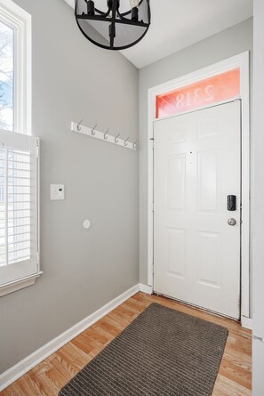 A hallway with a white door, a coat rack, a thermostat, and a doormat. - Cozy Downtown Escape (Indianapolis)