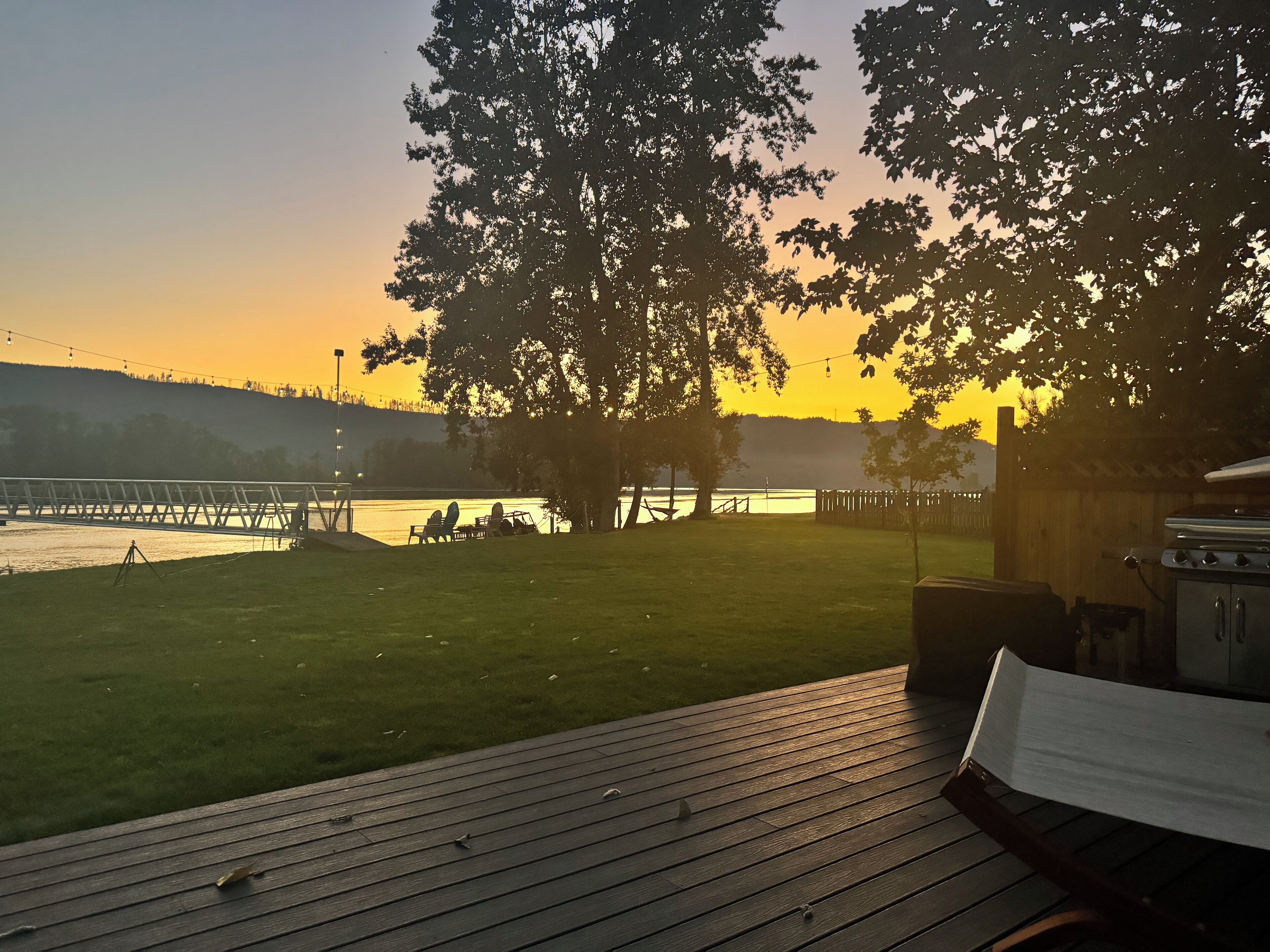 A deck with a grill and chairs overlooking a body of water at sunset.
