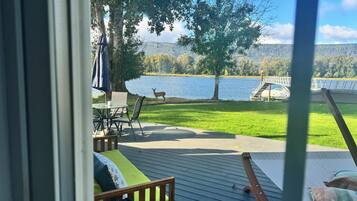 A deck with outdoor seating, a view of a lake, a deer, and a bridge.