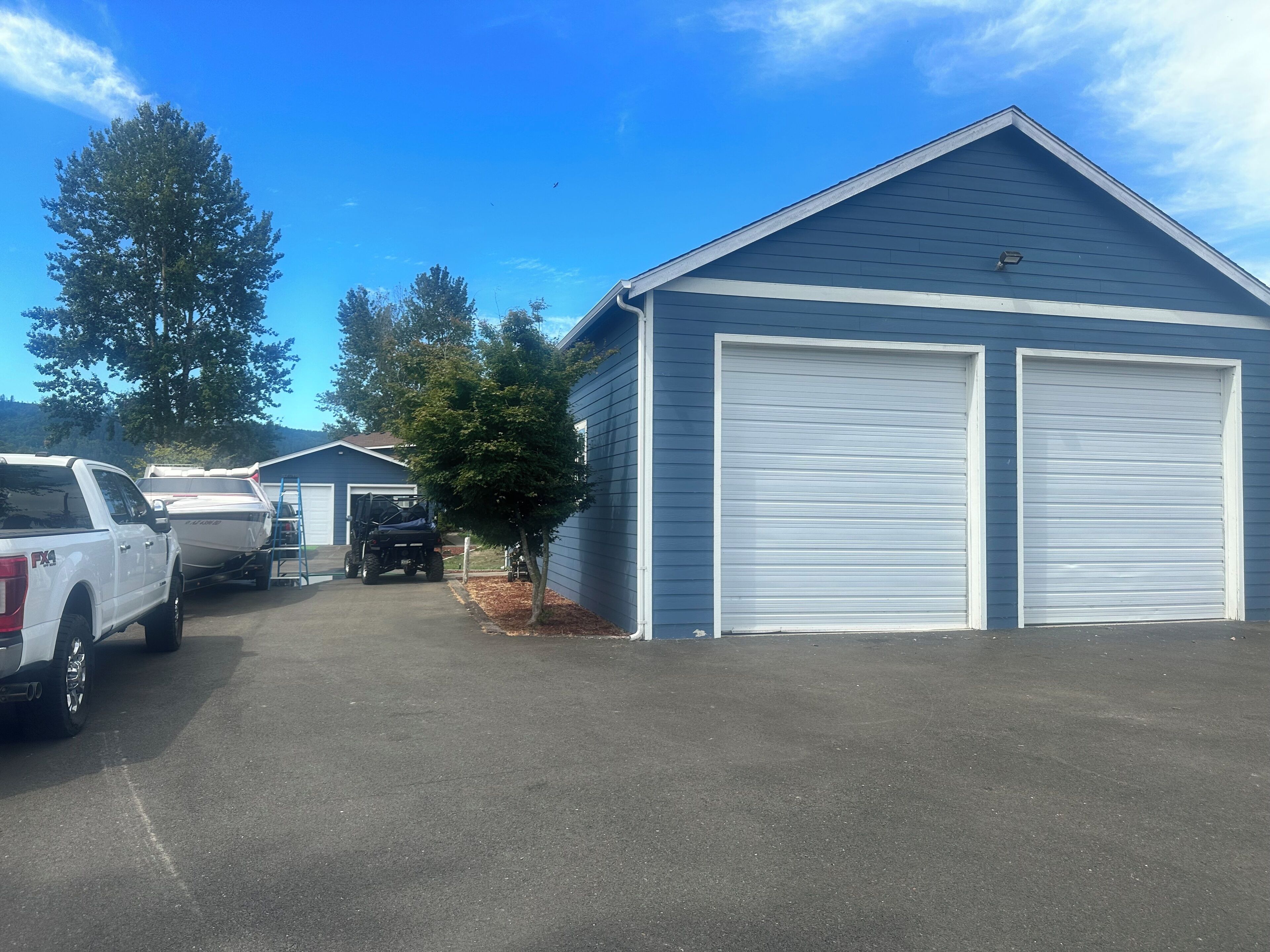 A garage with two large white roll-up doors, a white pickup truck, and a utility vehicle parked in front.