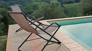 A poolside area with lounge chairs and a view of a hilly landscape.