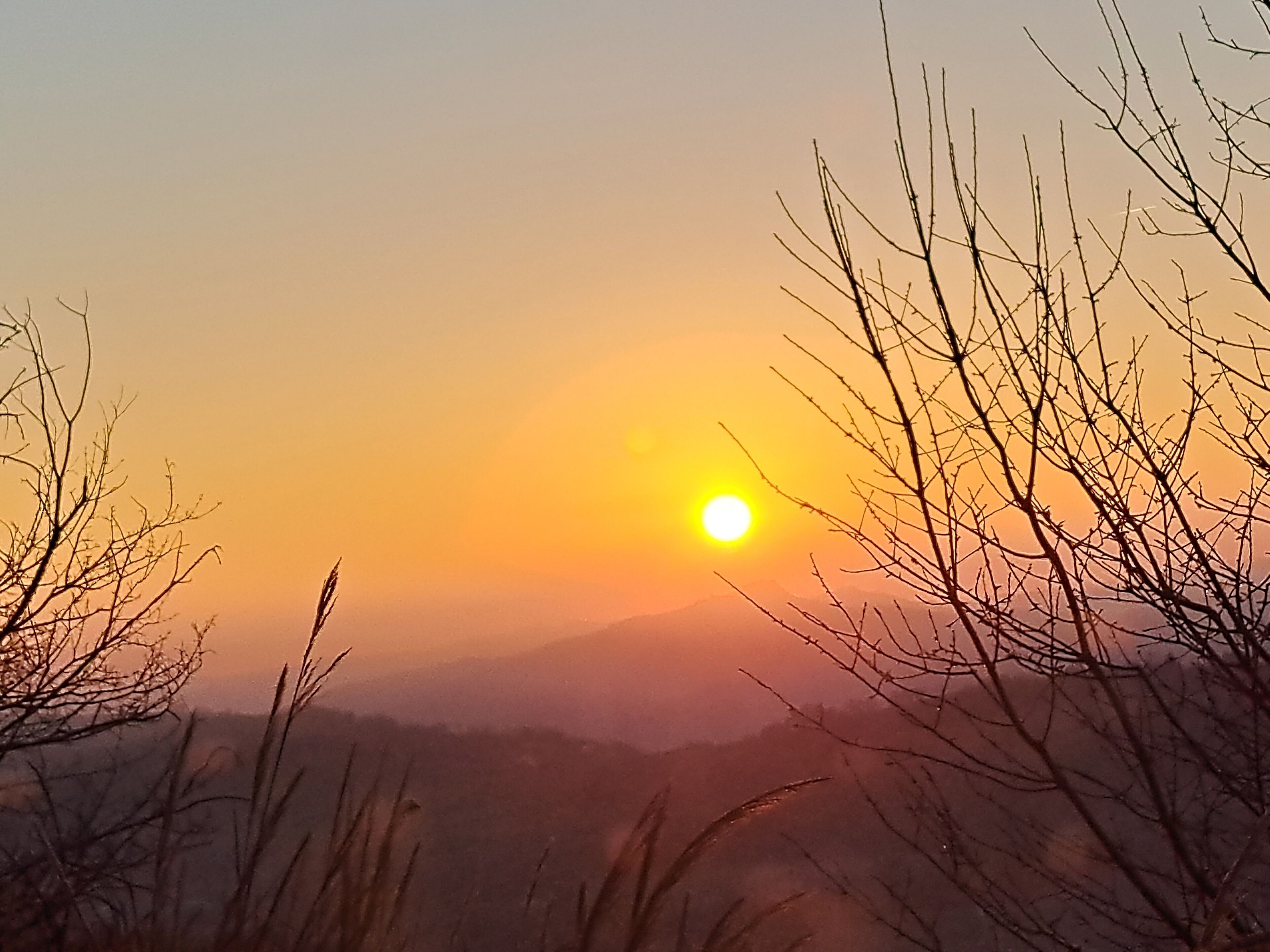 A sunset over a mountainous landscape with sparse vegetation.