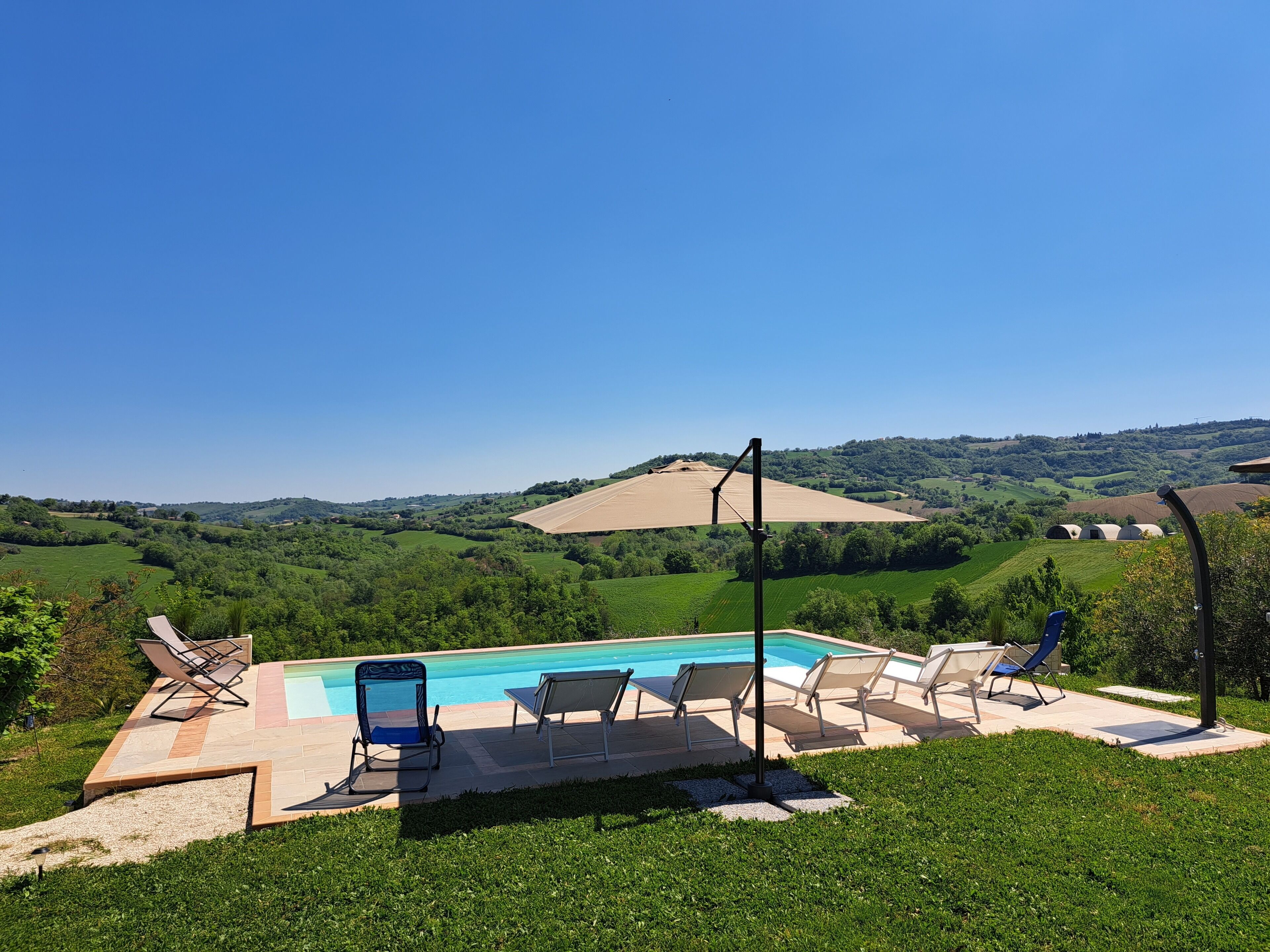 Una piscina con sillas de descanso, rodeada por un césped cuidado y una vista panorámica de colinas ondulantes y un campo extenso.