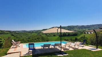 Una piscina con sillas de descanso, rodeada por un césped cuidado y una vista panorámica de colinas ondulantes y un campo extenso.