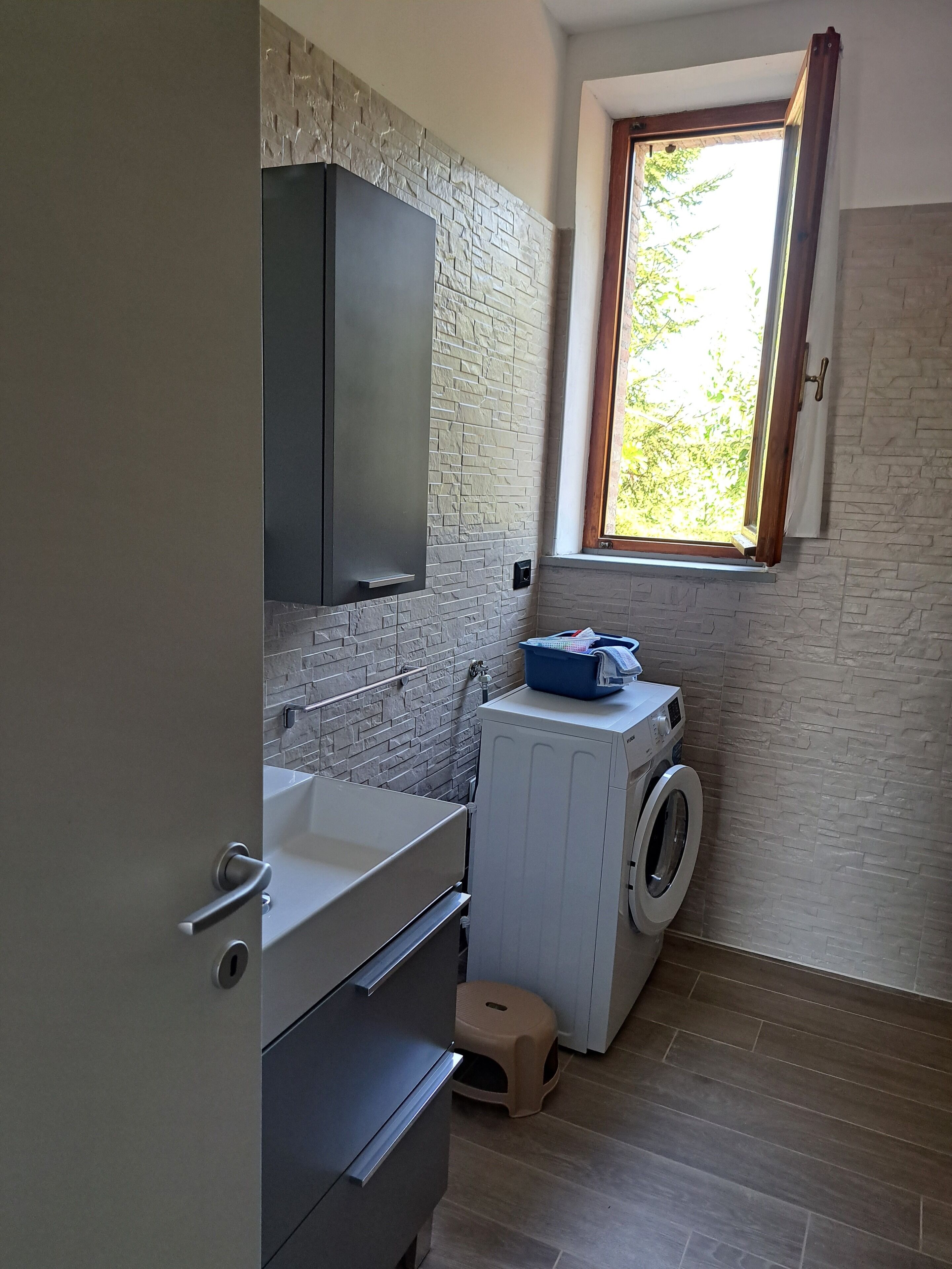 A compact laundry room with a washing machine, a drying rack, and a small stool.