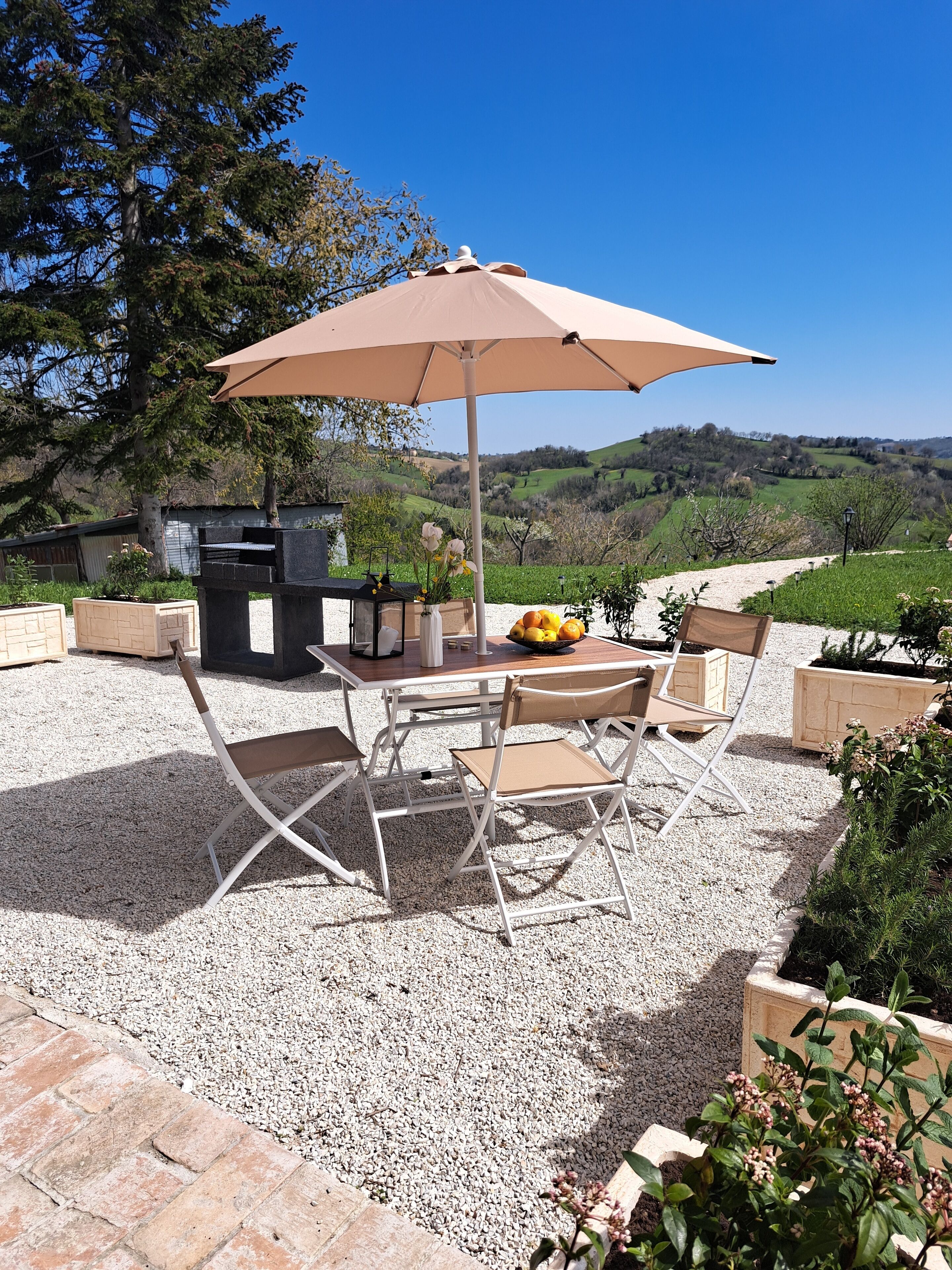 Une terrasse extérieure avec une table et des chaises, un grand parasol et une vue sur la campagne.