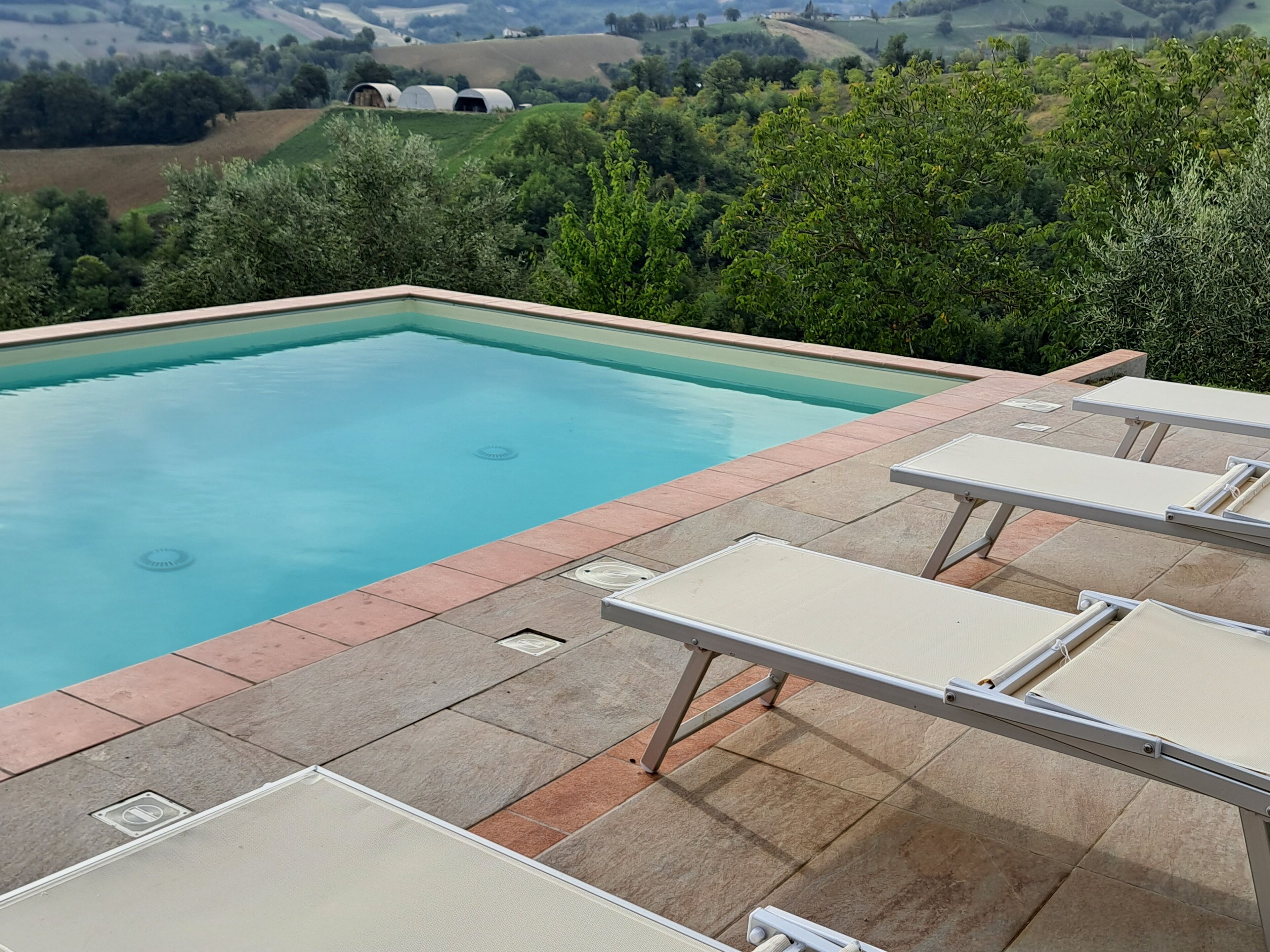 Una piscina con lettini e vista sulle dolci colline.