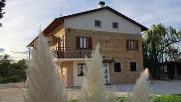 Una casa in pietra a due piani con un balcone, circondata da erba alta.