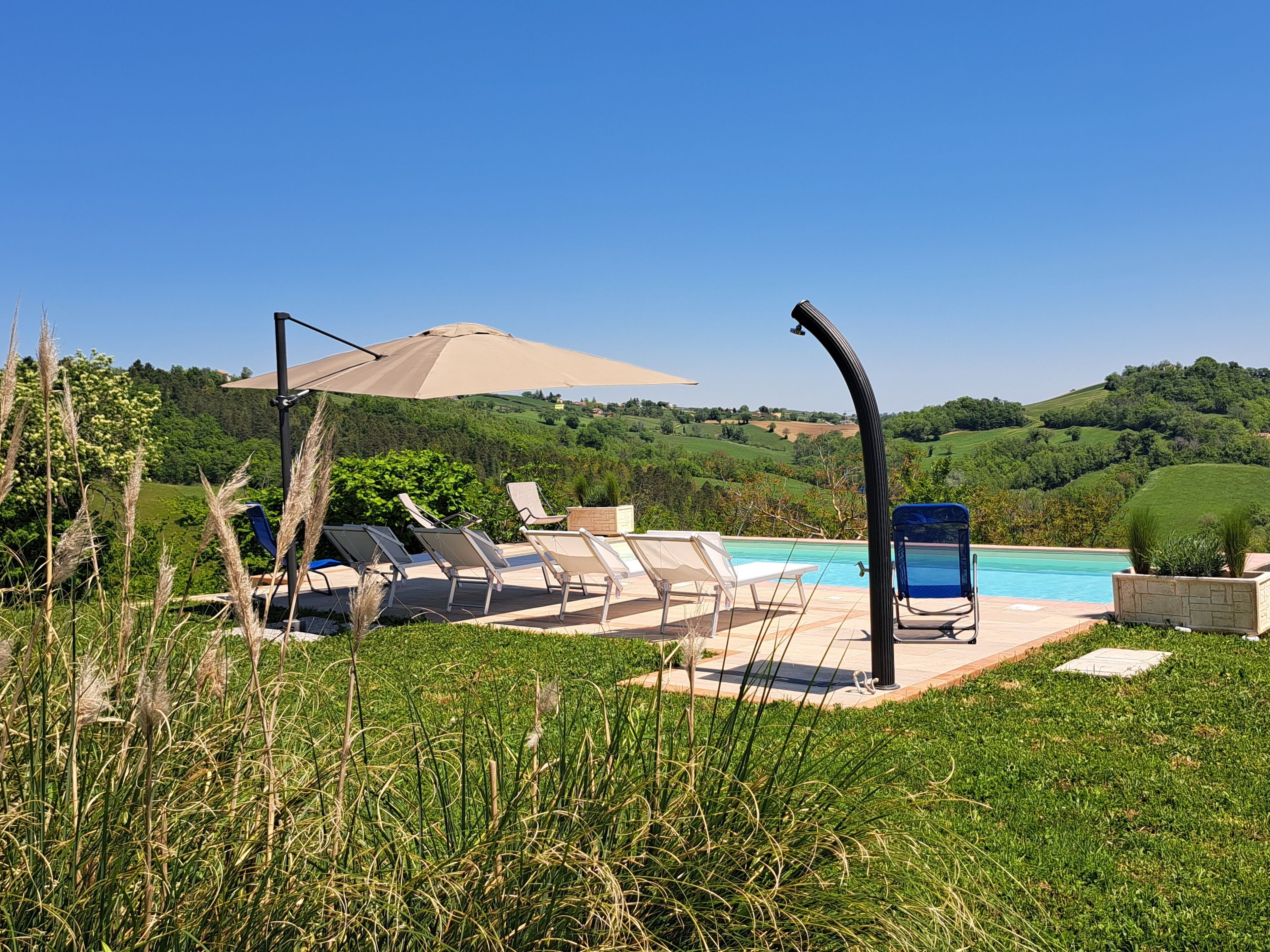 Ein Poolbereich mit Liegestühlen und Sonnenschirm, umgeben von üppiger Vegetation und sanften Hügeln im Hintergrund.