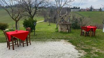 Un patio de grava con dos mesas y sillas de tejas rojas, rodeado de árboles y un paisaje cubierto de césped.