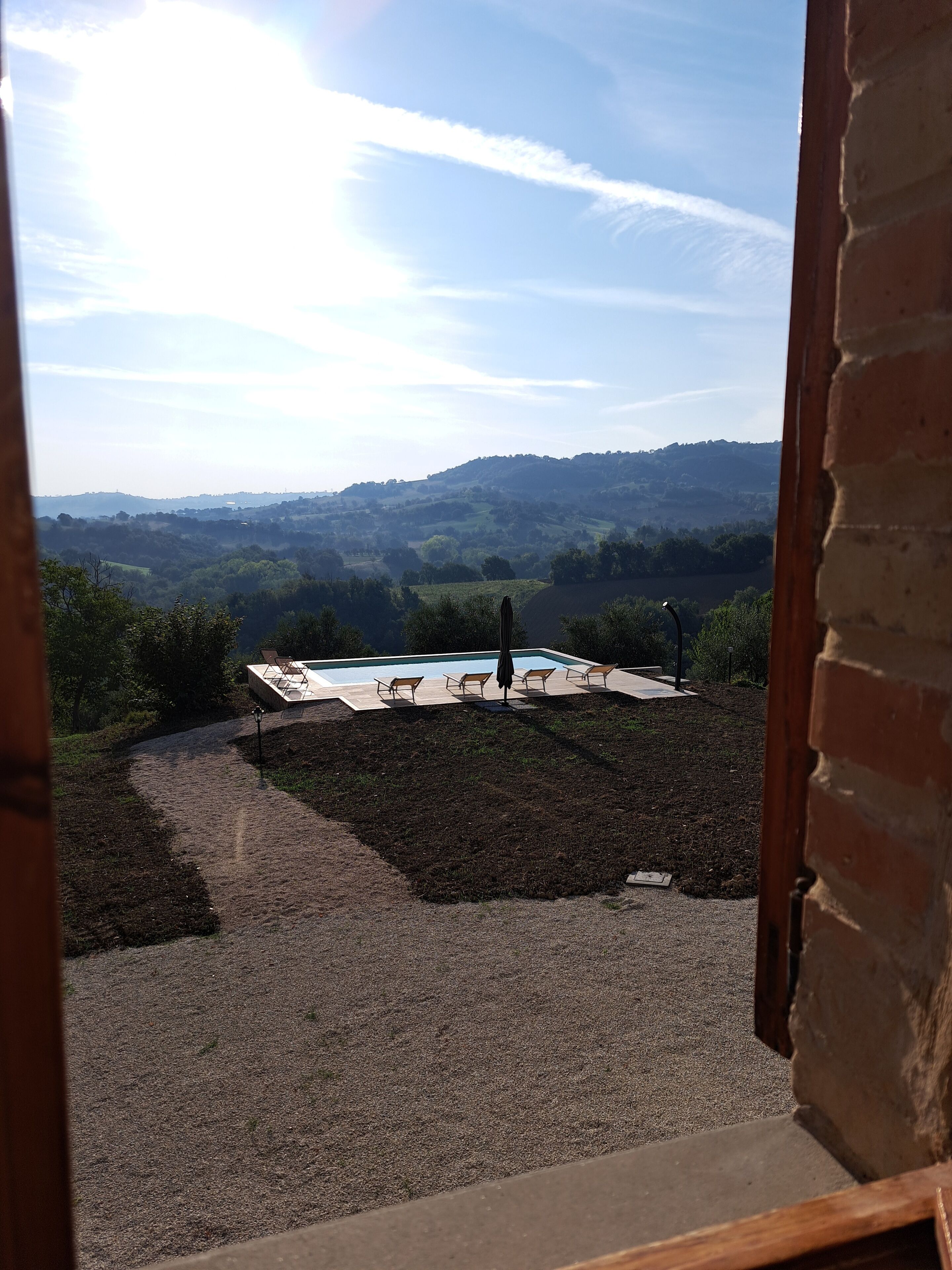 Vista desde una ventana sobre un área de piscina con un sendero de grava y un muro de ladrillo.