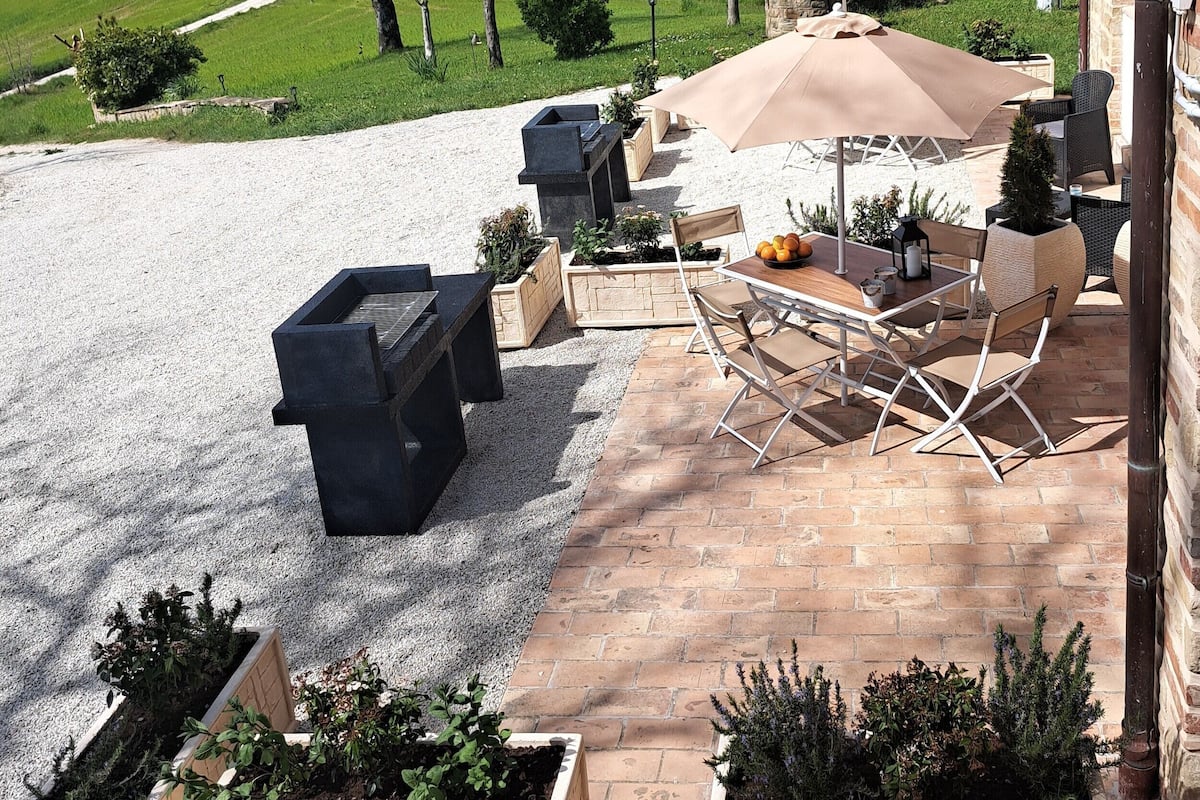 An outdoor patio with a table and chairs, surrounded by planters and a gravel area.